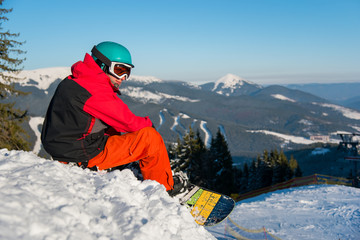 Fototapeta na wymiar Shot of a snowboarder enjoying beautiful view of snowy mountains, winter ski resort, relaxing on the edge of a slope looking around copyspace recreation travelling tourism