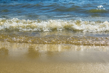 Soft waves on a sandy seashore. Sea beach on a sunny day, blue ocean water. Selective focus