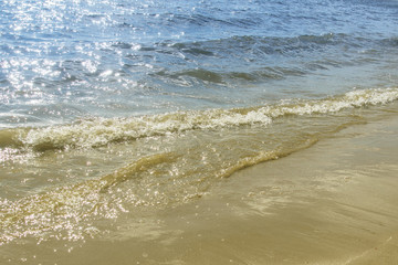 Soft waves on a sandy seashore. Sea beach on a sunny day, blue ocean water. Selective focus