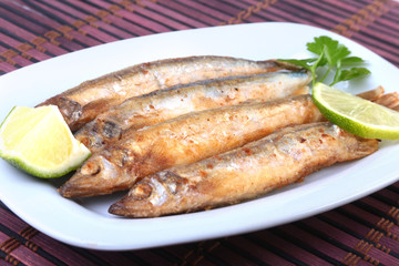 Deep frying small fish capelin and sliced lemon on white plate. Good snack to beer.