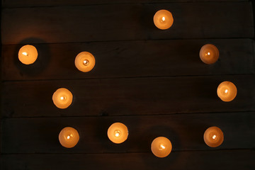 Burning candles  in the darkness. Small round tea light candles on wooden table top view.