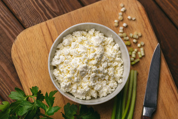 Cottage cheese in bowl and fresh herb on wooden cutting board on table. Healthy food