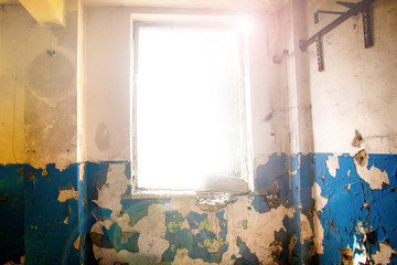 Gloomy and scary ruined room with pilled walls and broken window from which there is a bright light. The concept of freedom and hope