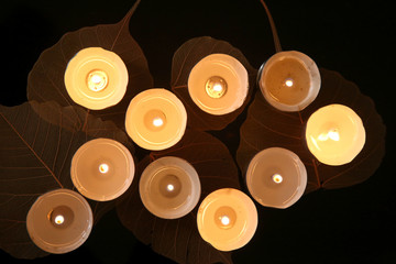 Burning candles with plant decorations  in the darkness. Small round tea light candles with leaves on black table.