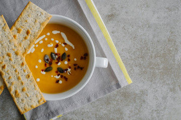 Pumpkin soup close up on light minimal background. Traditional seasonal fall and winter dish with cream and hot chilli on light grey concrete table top. Top view.