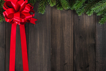 Christmas fir tree branches with red ribbon on dark rustic wooden background with copy space for text