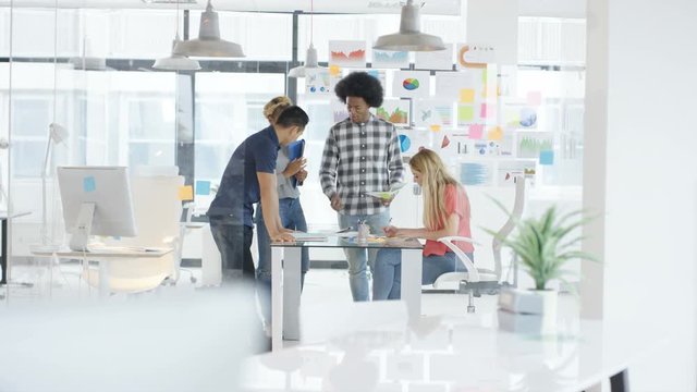  Young casual business group in a meeting in creative office with woman working on computer in foreground. Shot on RED Epic.