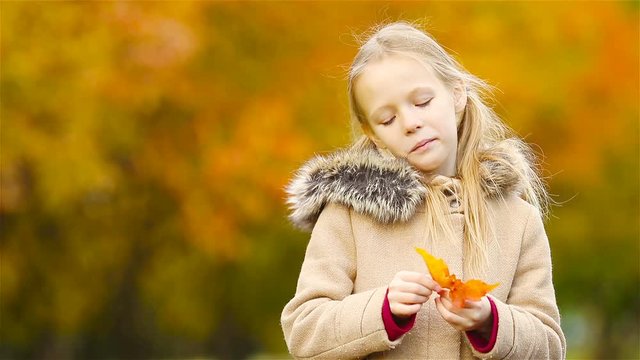 Portrait of adorable little girl outdoors at beautiful warm day with yellow leaf in fall