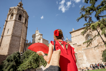 Young woman tourist in red dress walking on the central square near the main cathedral in Valencia city, Spain