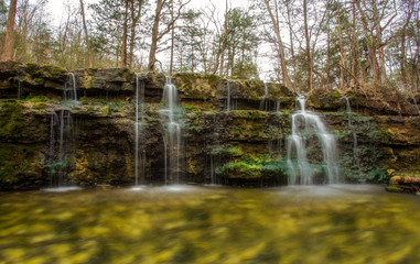 A soft small gentle waterfall over tall boulders in long exposure in a springtime forest landscape