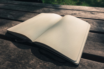 Blank empty moleskine notepad in three quarters view from top on wooden table in a park