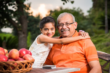 Young Indian girl embracing grandfather sitting in garden, Portrait of Indian grandfather and...