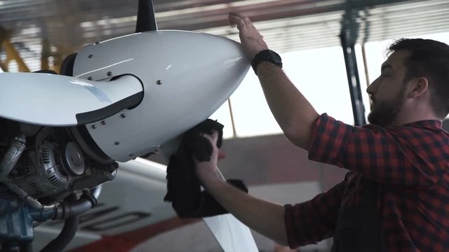 Bearded man polishing airplane propeller in hangar