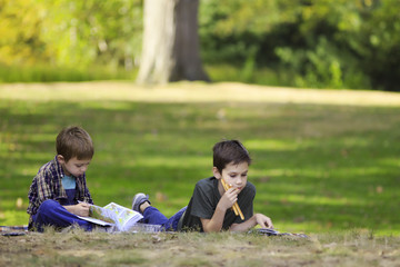 children lie on the grass and read books. boys eating breadsticks and reading outdoors. The concept...