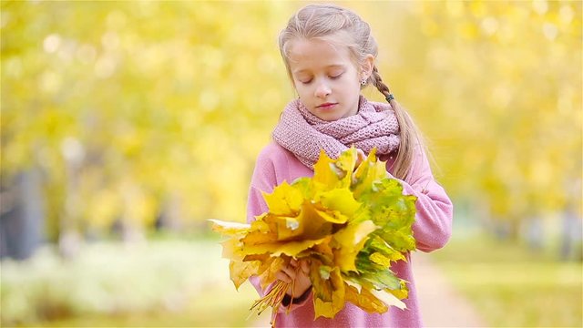 Portrait of adorable little girl with yellow and orange leaves bouquet outdoors at beautiful autumn day