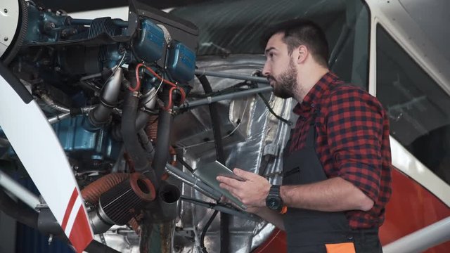 Aircraft mechanic carefully inspecting engine of plane using digital tablet.
