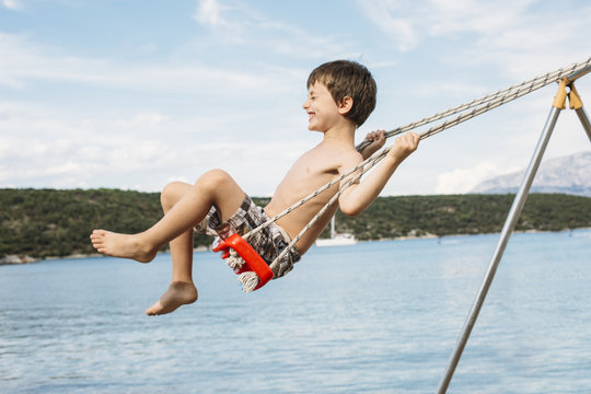 Boy swinging with closed eyes next to the sea