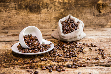 Fototapeta na wymiar Coffee beans in a white mug. Coffee beans on a wooden background. A bag of coffee beans. Dark background.