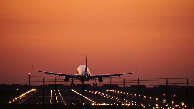 Airplane landing in silhouette against an orange sunset sky