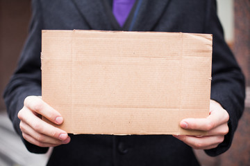 Unemployed businessman in an expensive suit with a blank cardboard sign on the street, close-up. Space for text.