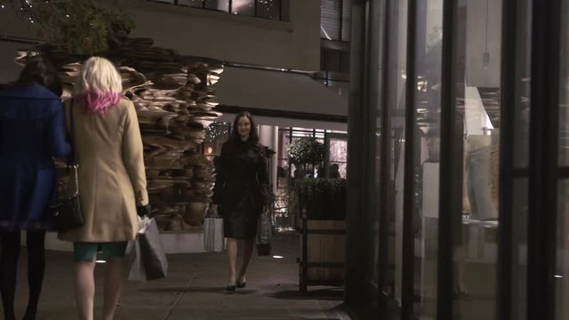  Young woman with shopping bags looking in shop window in the city at night