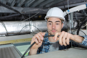 young handsome electrician wiring inside ceiling