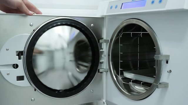 Hands are putting sets of dental instruments into autoclave for sterilization