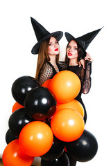 Two happy sexy women in black witch halloween costumes with orange and black balloon on party over white background