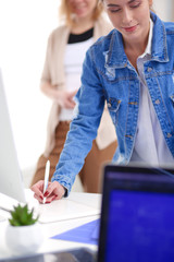 Two young woman standing near desk with instruments, plan and laptop.