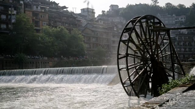 Handheld shot of water mill wheel on river on sunny day in Fenghuang Ancient Town, Guanxi County, China. Sustainable energy and water power traditional machinery, eco-friendly technology concept.