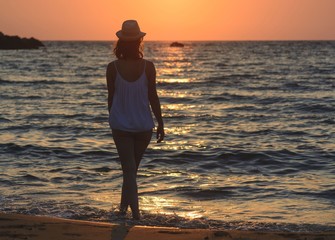 Fototapeta premium Young woman walking on the beach by the sea at summer sunset