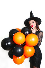 Portrait of beautiful young woman in black witch halloween costume with orange and black balloons over white background