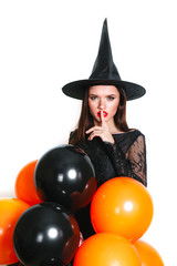 Portrait of beautiful young woman in black witch halloween costume with orange and black balloons over white background