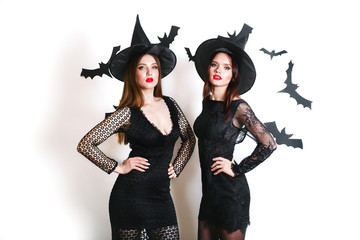 Two happy sexy women in black witch halloween costumes on party over white background
