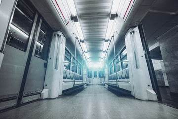 Wide-angle view from bottom of empty modern underground train car interior with doors opened: empty seats, rows of lamps following to vanishing point, electronic indicator of stations above the doors