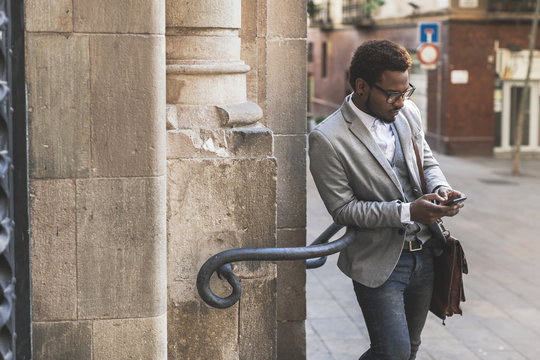 Young african american businessman typing with mobile phone on city streets.