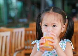 Closeup of little girl drinking Orange juice with looking camera.