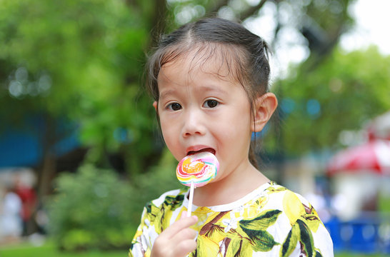 Little asian girl eating candy lollipop in the park.