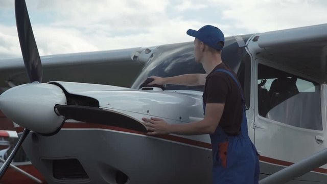 Young pilot or mechanic working on an aircraft wiping down the nose cowling on a small plane parked outdoors on an airfield