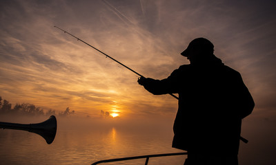 Fisherman throwing his rod, fishing from a little boat, beautiful morning sunrise scene