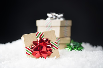 Small cardboard gift boxes with shiny holiday bows and striped ribbon sitting in snow, black background