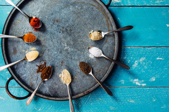 8 spices in spoons on a blue wooden tabletop