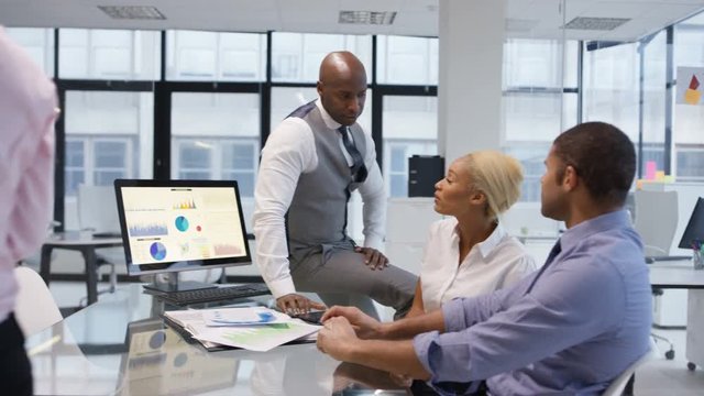 African American business team in a meeting looking at graphs and data on computer screen.