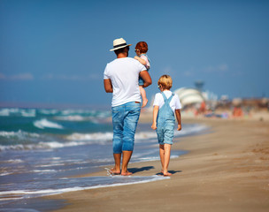 rear view of family, father with kids walking on sandy beach near the sea, summer vacation