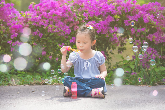 Little Asian Girl Sitting And Blowing Bubles In Park