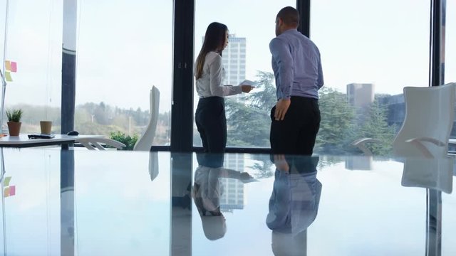  Business man & woman discussing paperwork in front of large office window