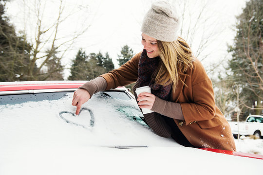 Young woman draws heart on windshield of car in winter
