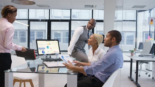 African American business team in a meeting looking at graphs and data on computer screen.