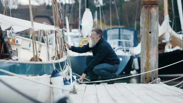  Mature bearded man mooring his boat to marina jetty after a sailing trip
