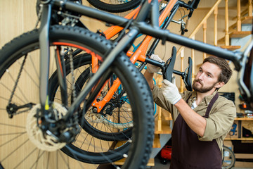 Fototapeta na wymiar Waist-up portrait of concentrated young mechanic in apron adjusting saddle height while working at modern bicycle repair shop